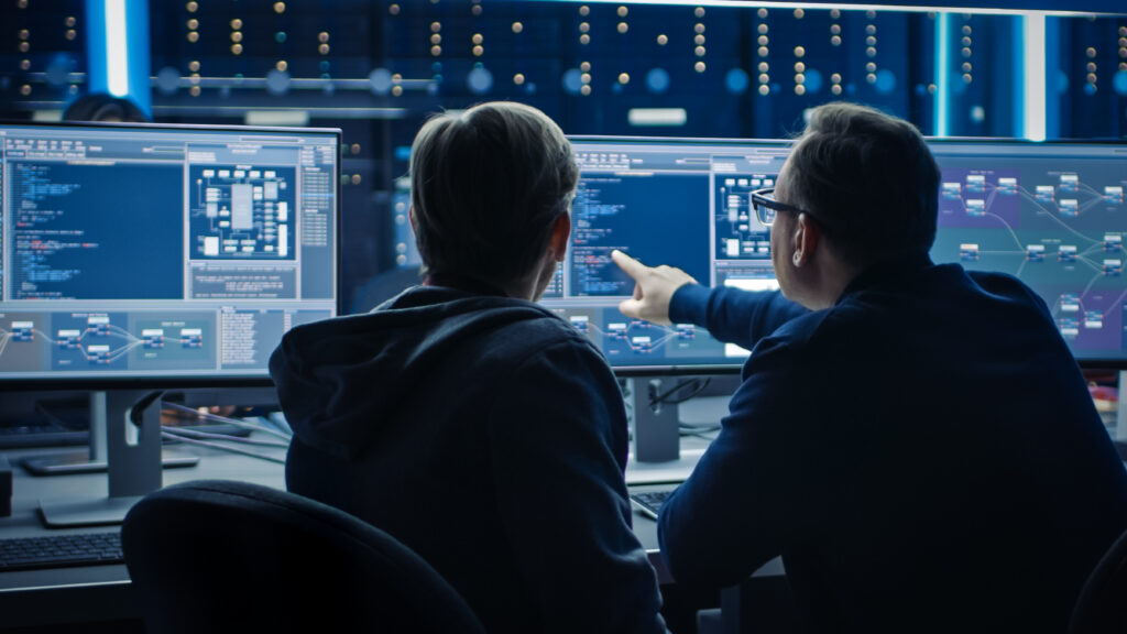 Deux programmeurs informatiques professionnels discutent de la conception et du développement de l'architecture du réseau de données de la blockchain sur un écran d'ordinateur de bureau. Département technique d'un centre de données en activité avec des racks de serveurs